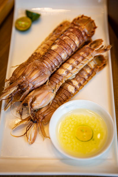 This dish features some grilled crawfish, presented on a white porcelain plate. The crawfish maintain their distinct segmented shell structure, exuding a tantalizing aroma. Alongside, a small ramekin of lemon butter sauce is provided, offering a complementary sweet and tangy flavor profile to the succulent crawfish meat.