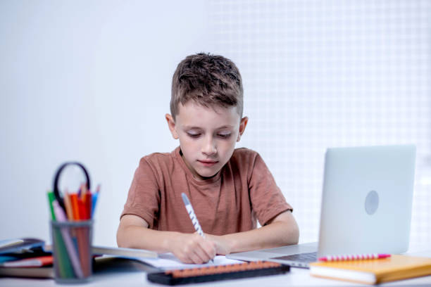 istock Cute pupil boy studying at home writing in exercise book doing homework, learning at home table 2161875926