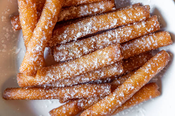 Person holding a plate of poffertjes, a traditional dutch treat, covered in powdered sugar and butter