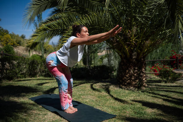 istock Woman practicing yoga outdoors on a sunny day, performing a standing forward bend pose in a garden setting. 2161885341