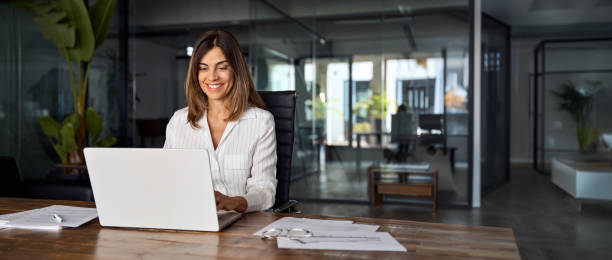istock Middle age European business woman CEO using laptop application for work at table workspace in office. Smiling Latin Hispanic mature adult professional businesswoman using pc digital computer. Banner 2161889983