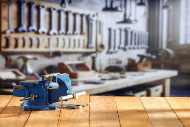 Mechanic bench vice on a wooden workbench in a craftsman's workshop. A blurred wall with tools in the background. Empty advertising space  for mounting products and objects.