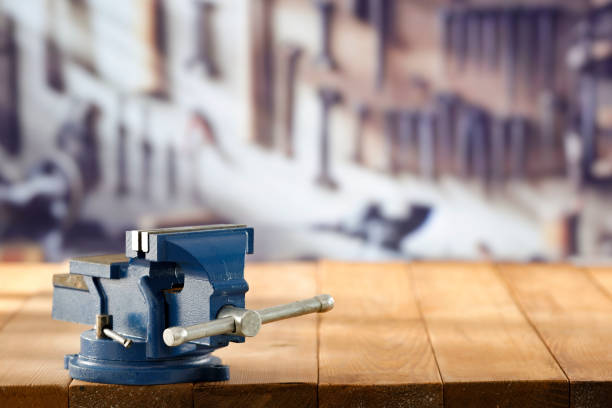 Mechanic bench vice on a wooden workbench in a craftsman's workshop. A blurred wall with tools in the background. Empty advertising space  for mounting products and objects.