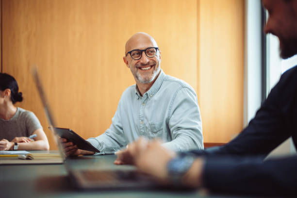 Smiling Businessman in Team Meeting with Colleagues in Office Mature businessman smiling during a meeting with colleagues. Team collaboration, professional setting, and modern business environment. group of people wearing eyeglasses stock pictures, royalty-free photos & images