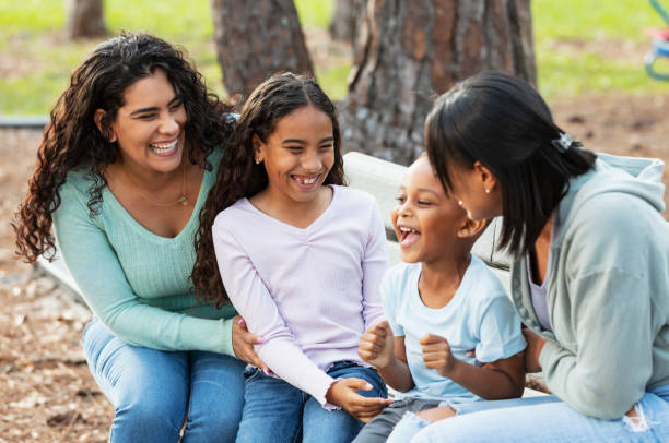 Two multiracial mothers, children laughing on park bench