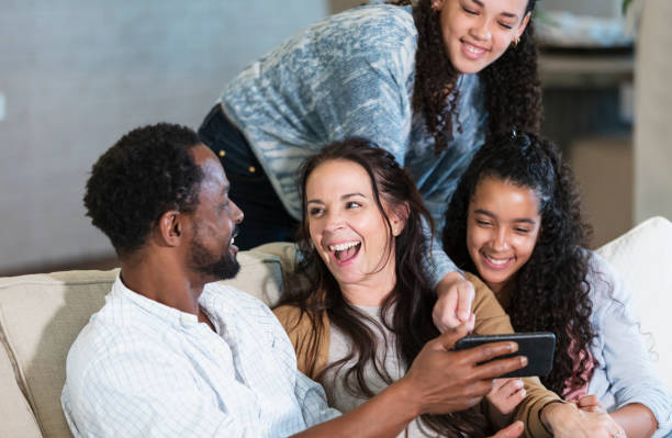 Multiracial family on sofa, laughing at mobile phone