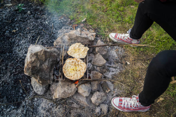 Bread, twisted on a skewer or stick, baked on fire. Barbecue food for party and camp. Image of a charcoal grill, close-up with live flames. Children's summer camp. Baking bread.