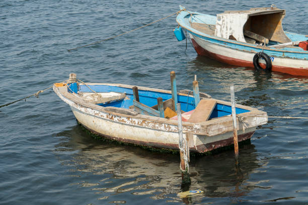 A detailed view of the weathered bow of a blue wooden boat, featuring a tied fender for protection. The worn textures and faded paint capture the essence of maritime life and its timeless charm. Perfect for themes of coastal living, nautical heritage, and rustic aesthetics.