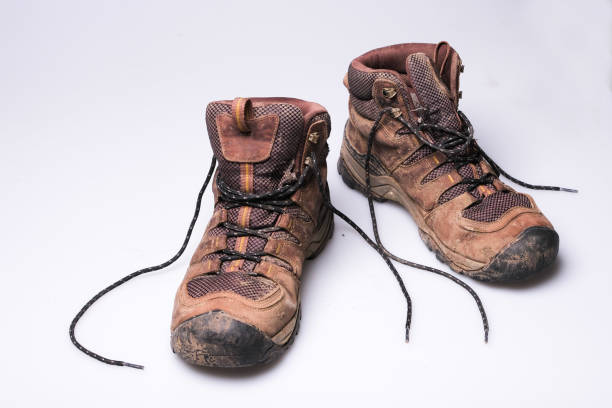 A pair of mans worn brown, muddy hiking boots on a plain white background
