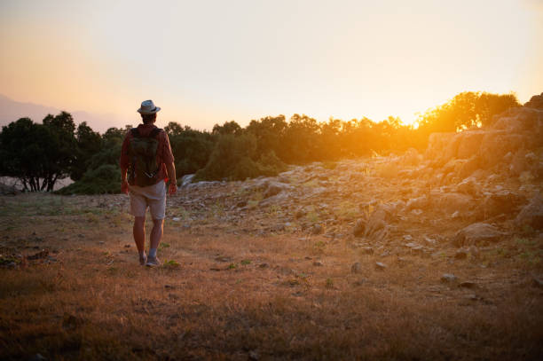 A backpacker wearing a hat and hiking gear explores a mountain landscape at sunset, reflecting the beauty of nature and the spirit of adventure.