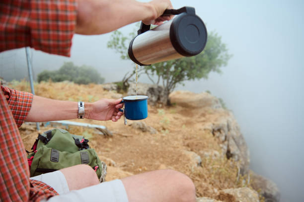 istock Man pouring coffee from thermos in blue cup while hiking on misty mountain 2161921668
