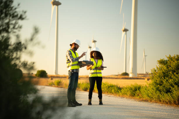 Two engineers analyzing data and planning new wind turbines on a wind farm, using a model and a digital tablet