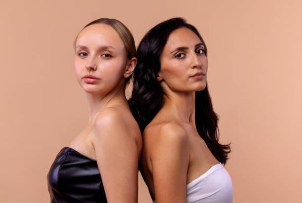 istock Two young diverse women wearing tops looking confident at camera while posing together on beige background. Charming models with natural makeup and perfect skin. 2161923066