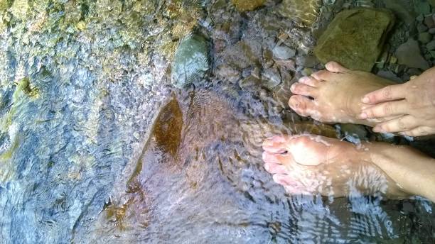 Feet relaxing and energizing in clear stream water with rocks in the background.