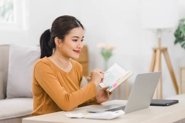 istock Smiling asian woman working on laptop while sitting in comfortable home with notebook and documents. 2161929769
