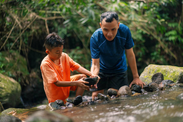 istock Pre Adolesence Boy Playing in Shallow River Building Rock Dam With Father 2161936290