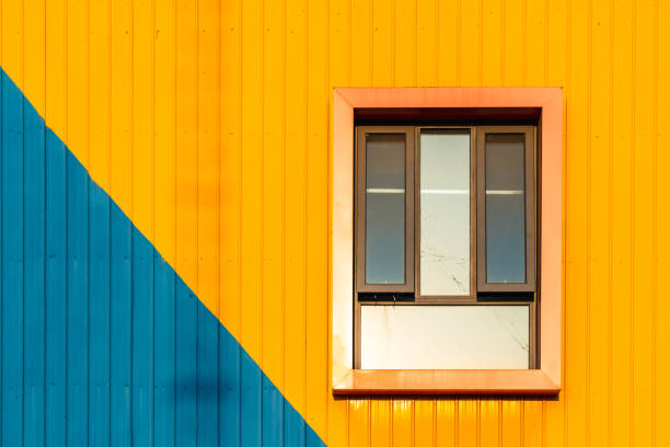 The wall is painted with blue and yellow in slanted color block. With a square-shaped window, the wall  shows a unique beauty of order and composition.