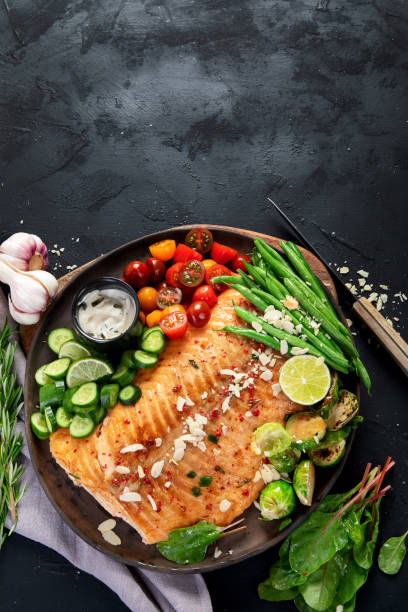 istock Cooked salmon with fresh vegetables, lime and souce. Baked fish on dark background 2161942875