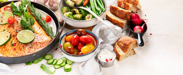 Grilled salmon and vegetables on wooden light background. Dinner table with cooked fish, tomatoes, asparagus