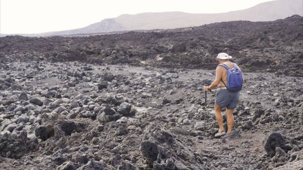 istock Senior Adventure: Man with Trekking Poles, Hat, and Backpack on Volcanic Trails 2161958153