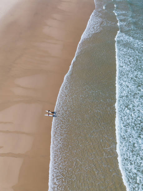 istock 2 Surfers standing on the sandy beach shore aerial view 2161967188