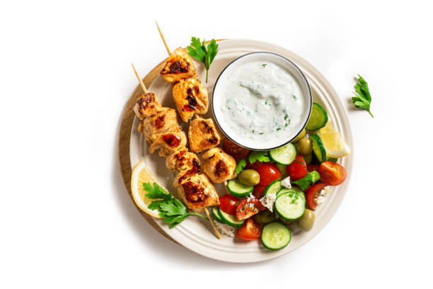 Grilled chicken kebab with fresh vegetable salad isolated on white background, top view. Mediterranean lunch with roasted skewers, tzatziki sauce and veggies, healthy food, design element.
