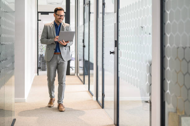 istock Male software developer smiling and doing online research over laptop while walking in office corridor 2161981203