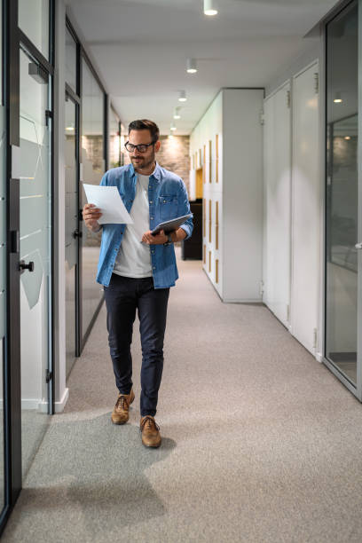 istock Full length of serious businessman with laptop analyzing project report while walking in office corridor 2161981237