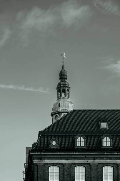 A historic building with a spire under a cloudy sky in a monochrome tone
