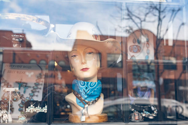 A manniquin with a western hat looks out from a retail storefront that reflects the buildings in downtown Boulder, Colorado.