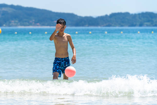 A mid-adult man and a boy dribble a boy by the water's edge.