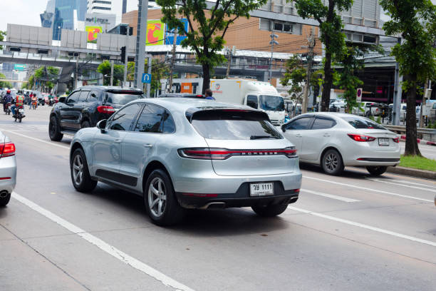 Porsche Macan driving in Bangkok captured in traffic on Ratchadaphisek Road in Bangkok near Fortune Mall and junction to Rama 9 Road. Other cars are driving on multiple lane street down towards downtown and Makkasan