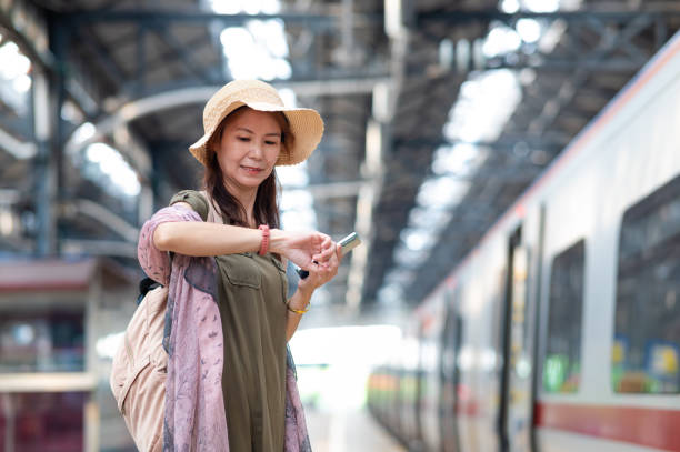 istock Asian woman checking her watch while waiting for train at the station platform 2162010651