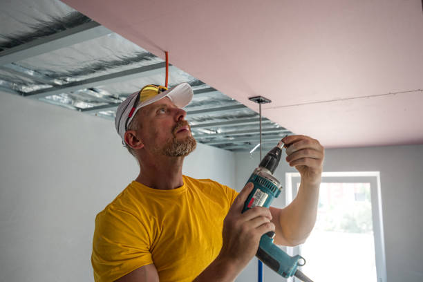 istock The worker screwing plasterboard to the ceiling. He is using special electric screwdriver and drywall lift. A red plasterboard improve the fire resistance of ceiling structures. 2162013519