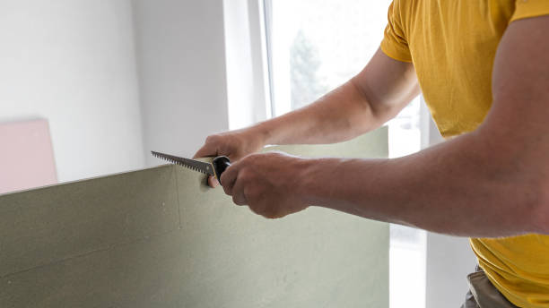 The worker make a plasterboard ceiling. He doing adjust the shape of the board with a drywall saw. A red plasterboard improve the fire resistance of ceiling structures.
