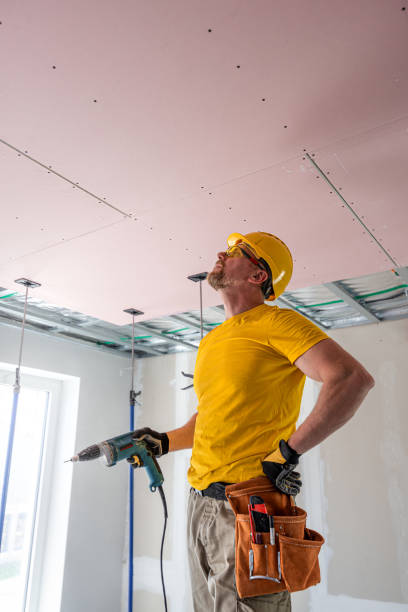 istock The worker screwing plasterboard to the ceiling. He is using special electric screwdriver and drywall lift. A red plasterboard improve the fire resistance of ceiling structures. 2162013607