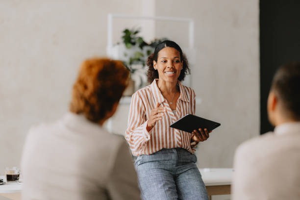 Group Business Meeting at Bright Beige Office Confident businesswoman leading a group business meeting at a bright beige office. Professional interaction and teamwork concept. advanced business development stock pictures, royalty-free photos & images
