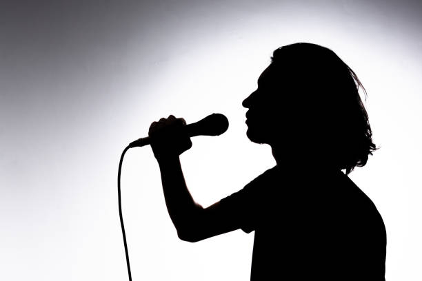 istock Silhouette of young singer holding wired microphone and singing with emotion. 2162036603