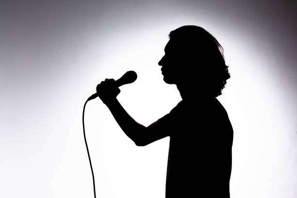 istock Silhouette of young singer holding wired microphone and singing with emotion. 2162036604