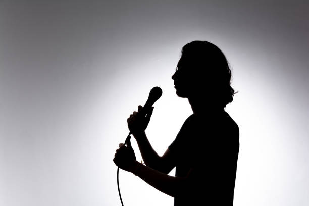 istock Silhouette of young singer holding wired microphone and singing with emotion. 2162036605
