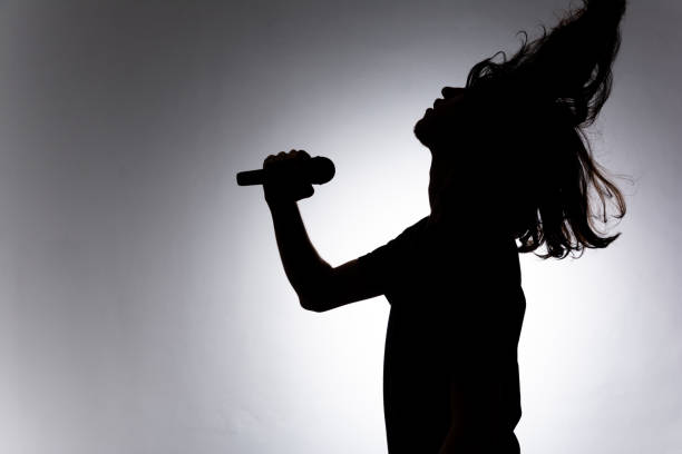 istock Silhouette of young man holding wireless microphone singing music with emotion. 2162036609