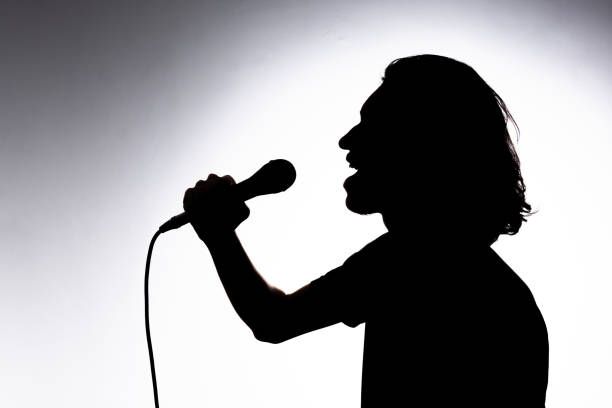 istock Silhouette of young singer holding wired microphone and singing with emotion. 2162036614