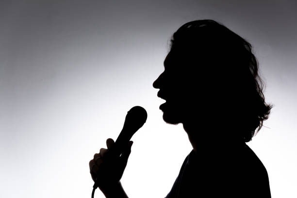 istock Silhouette of young singer holding wired microphone and singing with emotion. 2162036639