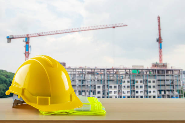 Yellow safety construction helmet on wood table with construction site background