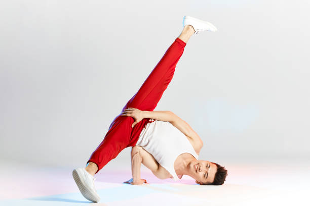 young Korean male dancer executing basic freezes of downrock break, showing the dance moves of contemporary dance in sportive red sweatpants for sports on white studio background