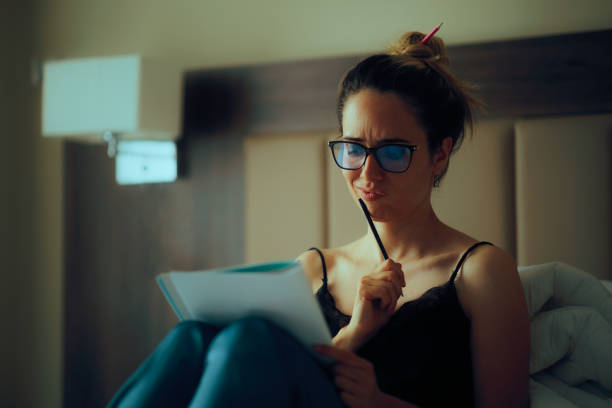 Cropped shot of young woman sits on bed, makes notes in diary, focused looking aside. Blogger create publication for blog in notebook. Copy space