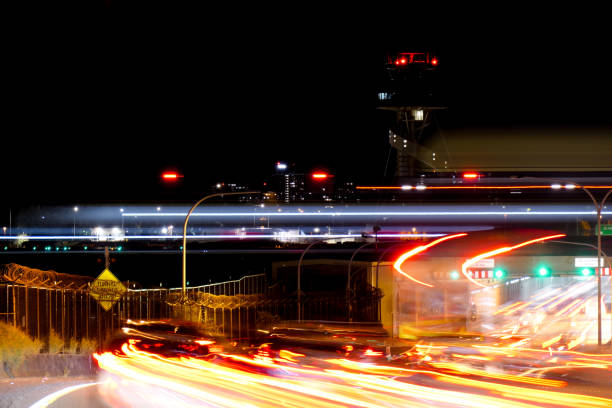 The fuselage and vertical stabiliser lights of a Singapore Airlines Airbus A350-941 plane, registration 9V-SJE, cuts across the image as she lands on the main runway of Sydney Kingsford-Smith Airport. Beneath are light beams of taillights and headlights of cars travelling through the tunnel under the runway.   Lights of the air traffic control tower are visible on the right.  This image was achieved with a 5 second exposure and taken from near Kyeemagh Avenue, Kyeemagh on a cold night on 13 July 2024.
