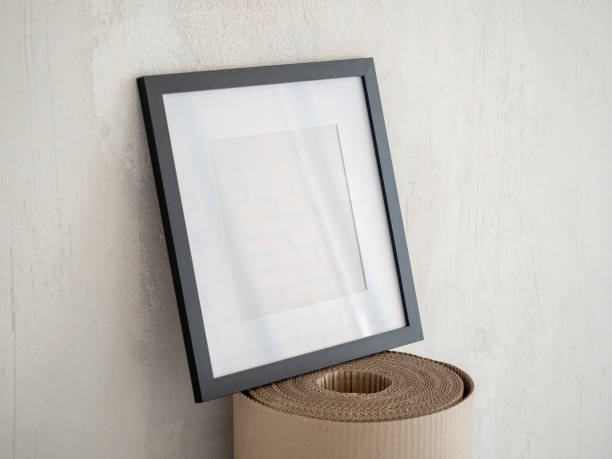 istock Square poster with black frame mockup standing on a roll of cardboard kraft paper 2162074576
