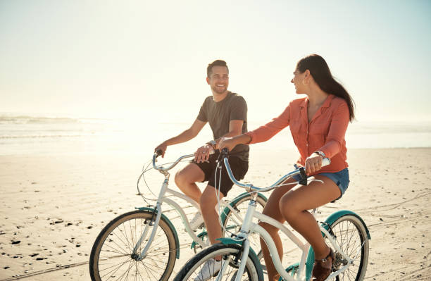 Young happy couple riding bicycles together at the beach