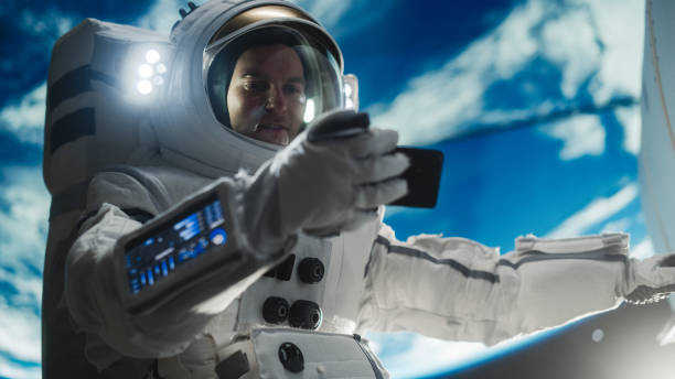 istock Male Astronaut Holding Smartphone in Horizontal Position, Watching a Video on a Device in Open Space Outside Earth Atmosphere. Professional Engineer Undertaking Satellite Service and Maintenance Job 2162077499